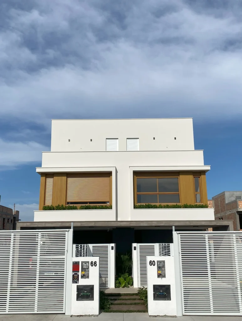 Fachada frontal da obra concluída, com dois acessos independentes, portões de lâminas brancas e painéis de madeira clara no pavimento superior