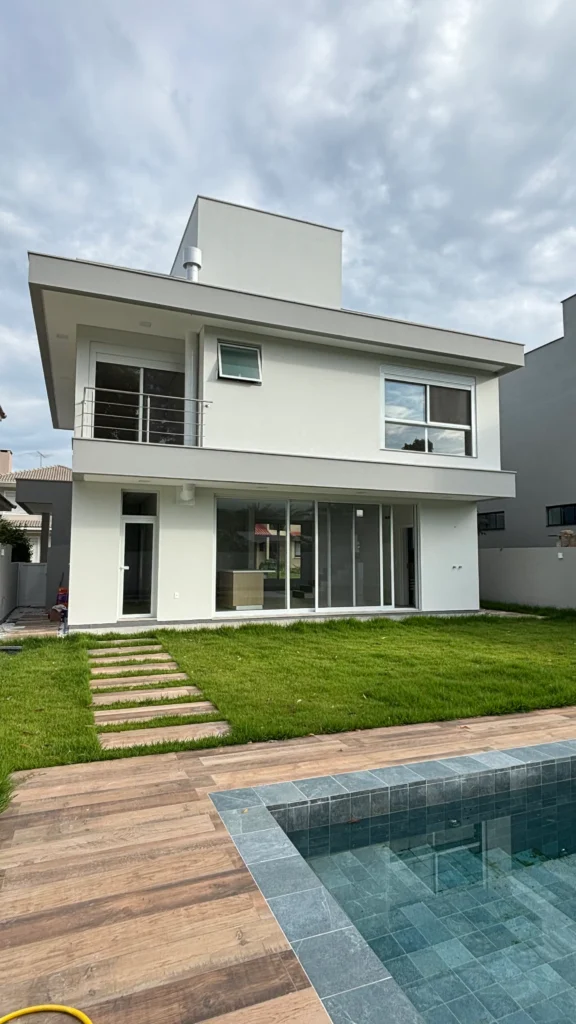 Foto da obra concluída em perspectiva dos fundos, com o deck de madeira e a piscina revestida em pastilha verde