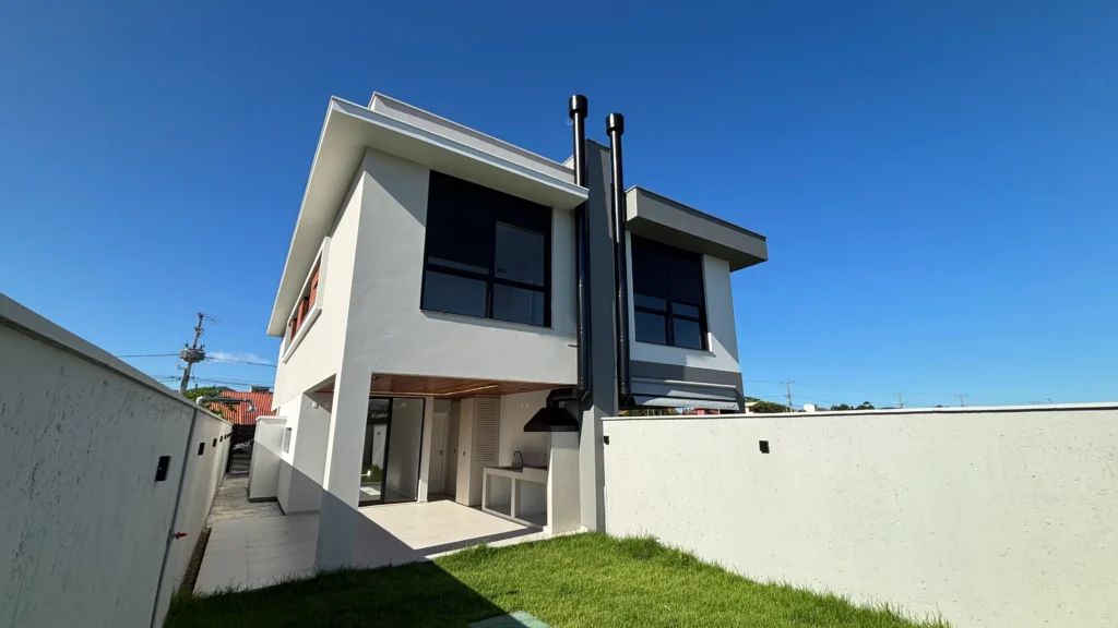 Perspectiva dos fundos da obra concluída, com área coberta voltada para o gramado e chaminés verticais no perfil da cobertura