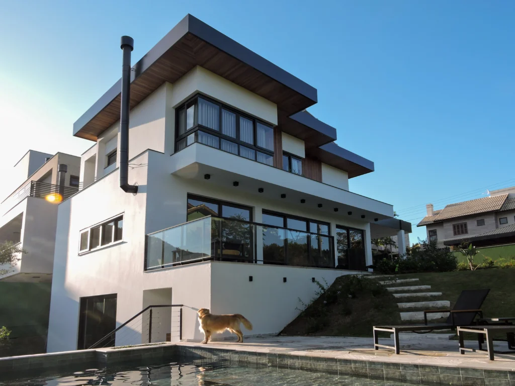 Perspectiva dos fundos, com a piscina no pátio, o guarda-corpo de vidro do terraço e a escada de acesso ao gramado