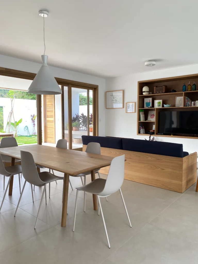 Sala de jantar integrada, com mesa de madeira, cadeiras brancas e estante ao fundo
