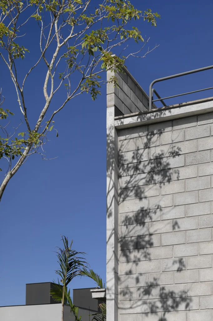 Detalhe da fachada frontal, com a textura do bloco de concreto e a sombra da árvore