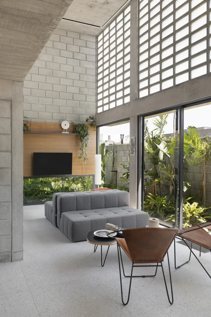 Sala de estar com parede de elementos vazados, sofá modular cinza e poltronas de couro