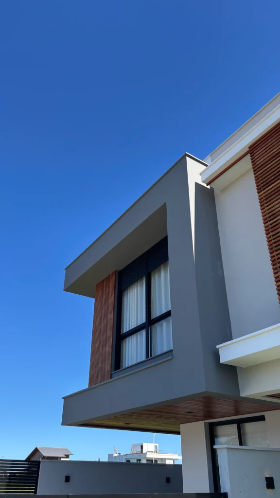 Perspectiva da obra concluída vista de baixo, destacando o balanço do volume superior e o painel ripado de madeira