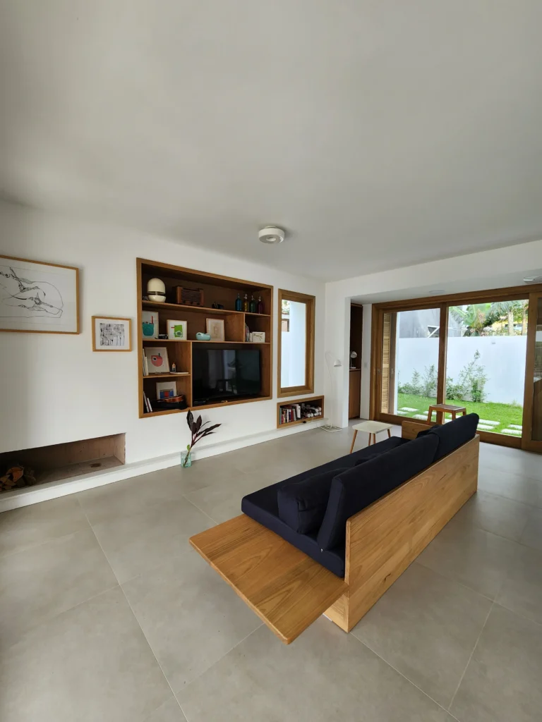 Sala de estar com estante de madeira embutida, sofá de madeira com almofadas azuis e piso claro