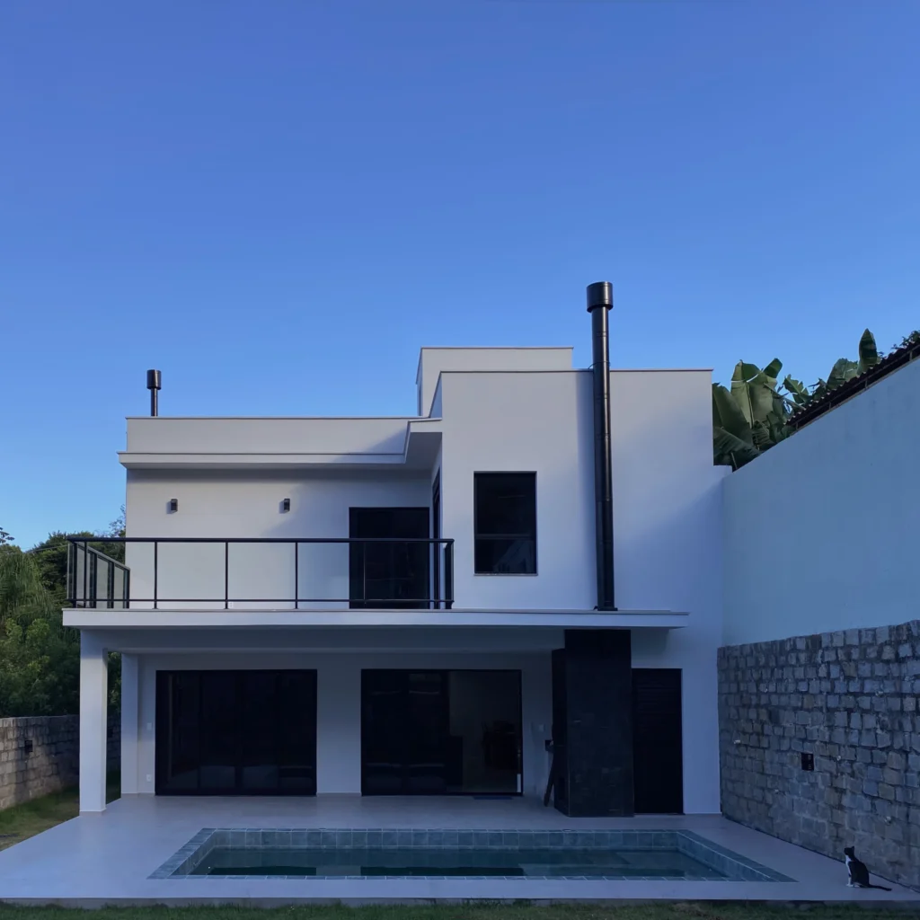 Fachada posterior, com área coberta sob o pavimento superior, piscina no pátio e muros de pedra