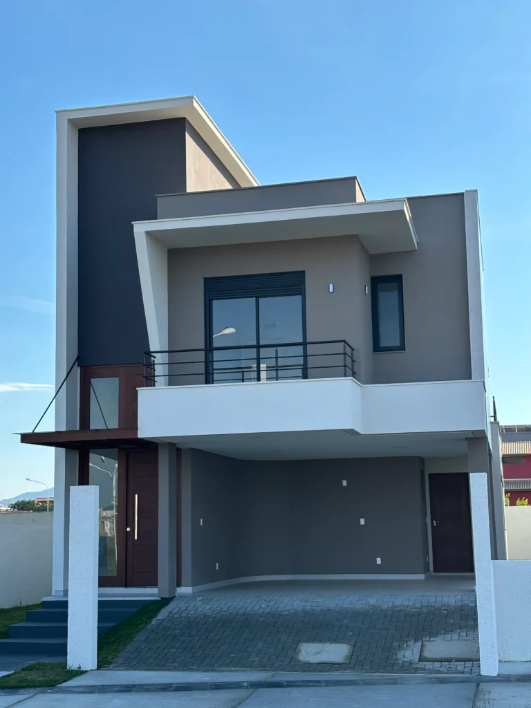 Fachada frontal da obra concluída, com volume em grafite ao fundo, sacada branca projetada e garagem no térreo