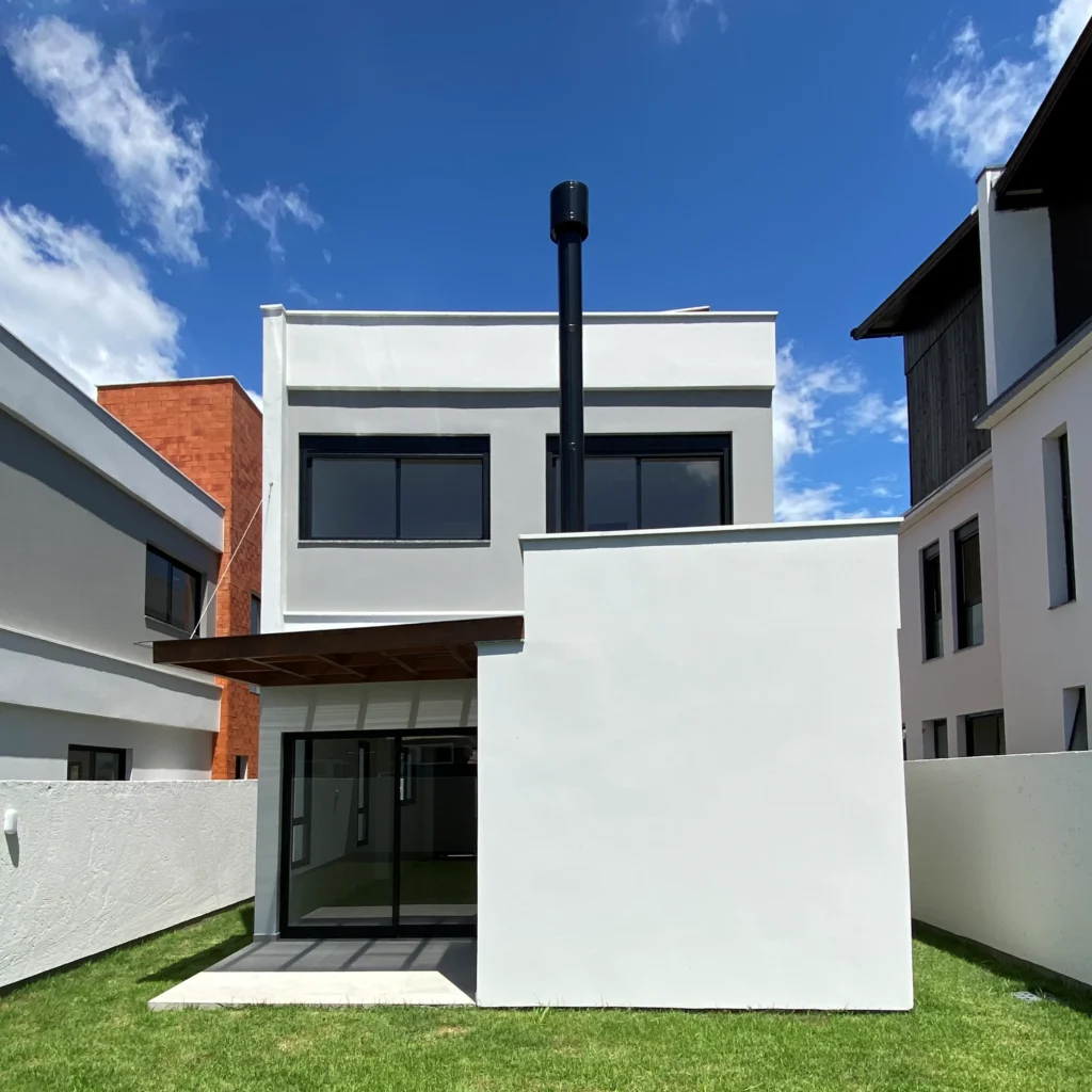 Foto da obra concluída, perspectiva posterior da casa 02, com o volume branco avançando sobre o gramado
